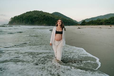 Gestante caminhando na areia durante ensaio fotográfico na Praia de Itamambuca em Ubatuba.'