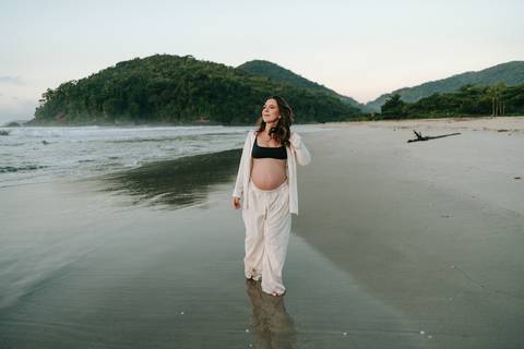 Gestante caminhando na areia durante ensaio fotográfico na Praia de Itamambuca em Ubatuba.'