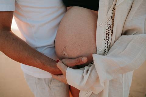 otografia de gestante em Ubatuba destacando a barriga durante ensaio na praia.'