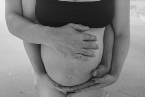 otografia de gestante em Ubatuba destacando a barriga durante ensaio na praia.'