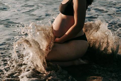 otografia de gestante em Ubatuba destacando a barriga durante ensaio na praia.'