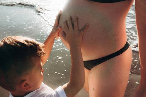 otografia de gestante em Ubatuba destacando a barriga durante ensaio na praia.'