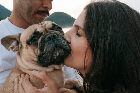 Gestante e seu cachorro compartilhando um momento de carinho durante ensaio fotográfico na praia.'
