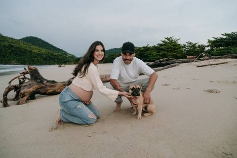 Ensaio gestante na praia com cachorro da família, registrado com luz natural em Ubatuba.'