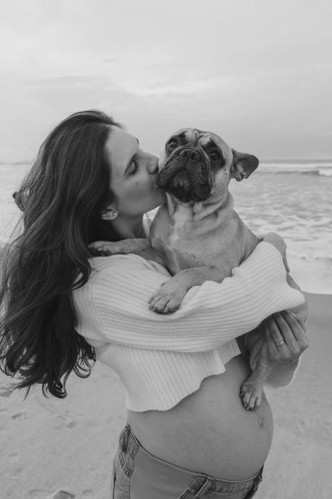 Mulher grávida abraçando seu cachorro durante ensaio gestante ao ar livre em Ubatuba.'