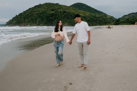 Casal caminhando na areia durante ensaio fotográfico gestante na Praia de Itamambuca em Ubatuba.'