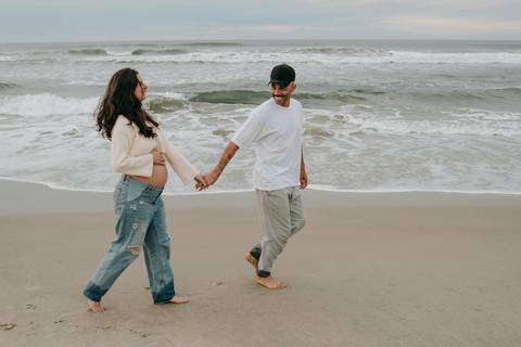 Casal caminhando na areia durante ensaio fotográfico gestante na Praia de Itamambuca em Ubatuba.'