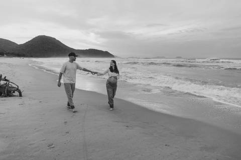Casal caminhando na areia durante ensaio fotográfico gestante na Praia de Itamambuca em Ubatuba.'
