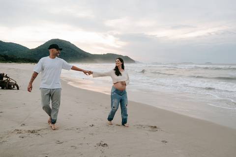Casal caminhando na areia durante ensaio fotográfico gestante na Praia de Itamambuca em Ubatuba.'