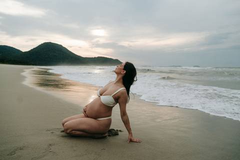 Gestante com seu cachorro durante ensaio fotográfico na praia de Ubatuba ao pôr do sol.'