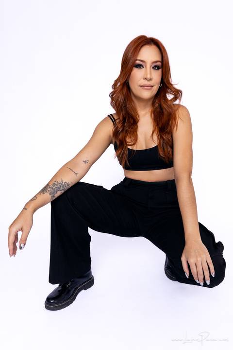  mulher agachada no chão com mãos na frente das perna usando blaze preto, top e calça cargo, no fundo branco para retrato feminino em estudio fotografico para fotos corporativas em natal'