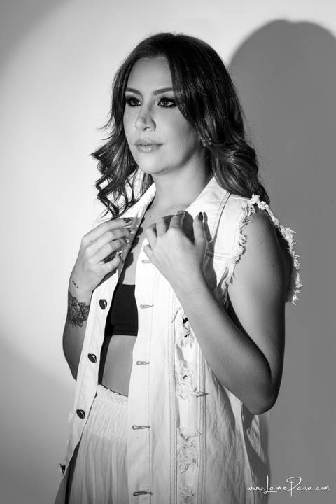  mulher em pé olhando para o lado, seria e com mãos em gola de colete, usando top preto, calça cargo e colete off white, no fundo branco para retrato feminino em estudio fotografico para fotos corporativas em natal'