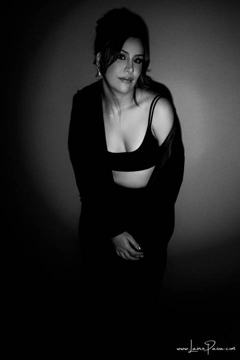  mulher encostada na parede em pé com mãos nas pernas usando blaze, top e calça cargo preta, no fundo vermelho para retrato feminino em estudio fotografico para fotos corporativas em natal'