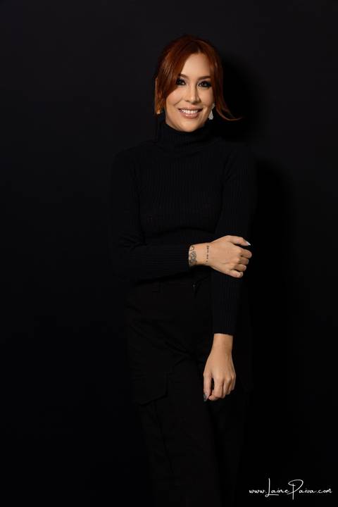  mulher em pé com mão no braço usando blusa gola alta e calça cargo preta, no fundo cinza para retrato feminino em estudio fotografico para fotos corporativas em natal'