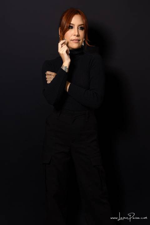  mulher em pé com mãos no rosto usando blusa gola alta e calça cargo preta, no fundo cinza para retrato feminino em estudio fotografico para fotos corporativas em natal'