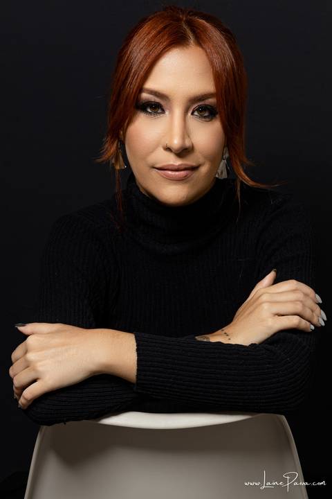  mulher sentada em cadeira com braços cruzados usando blusa gola alta e calça cargo preta, no fundo cinza para retrato feminino em estudio fotografico para fotos corporativas em natal'