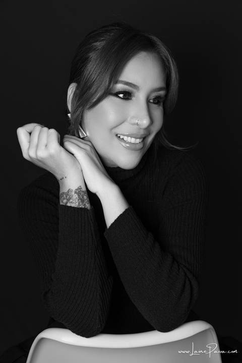  mulher sentada em cadeira com braços cruzados e olhando para o lado usando blusa gola alta e calça cargo preta, no fundo cinza para retrato feminino em estudio fotografico para fotos corporativas em natal'