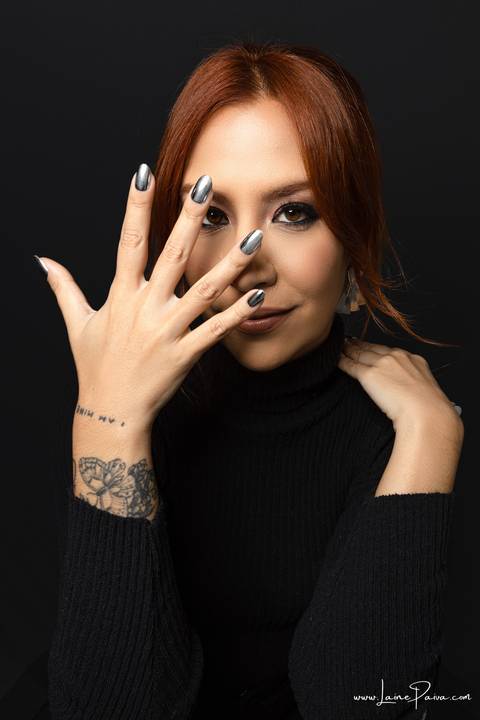  mulher mostrando unha prata e uma mão na frente do rosto e outra encostada no ombro olhando para frente usando blusa gola alta e calça cargo preta, no fundo cinza para retrato feminino em estudio fotografico para fotos corporativas em natal'