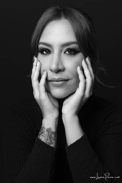 mulher olhando para frente e com mãos no rosto usando blusa gola alta e calça cargo preta, no fundo cinza para retrato feminino em estudio fotografico para fotos corporativas em natal'