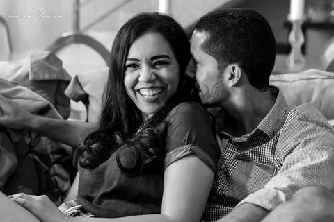 homem beijando pescoço de mulher que sorrir enquanto estão sentados no sofa da sala do loft de macamirim'