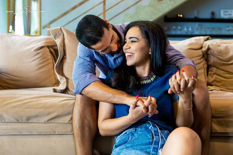 homem sentado no sofá e mulher no chão da sala do loft de macamirim se olhando e rindo'