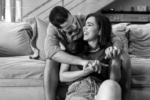 homem sentado no sofá e mulher no chão da sala do loft de macamirim se olhando e rindo'