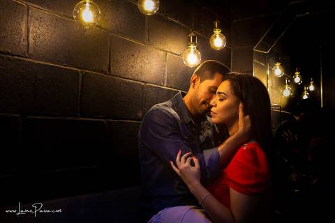 homem sentado e pegando no pescoço de mulher como se fosse a beijar com luzes sob suas cabeças em banheiro escuro do loft de macamirim'