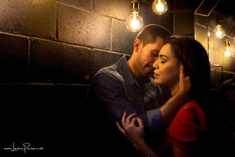 homem sentado e pegando no pescoço de mulher como se fosse a beijar com luzes sob suas cabeças em banheiro escuro do loft de macamirim'