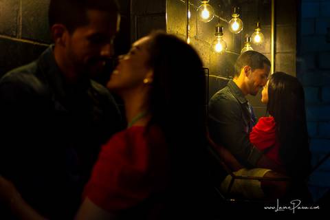 homem sentado e pegando no pescoço de mulher como se fosse a beijar com luzes sob suas cabeças em banheiro escuro do loft de macamirim'