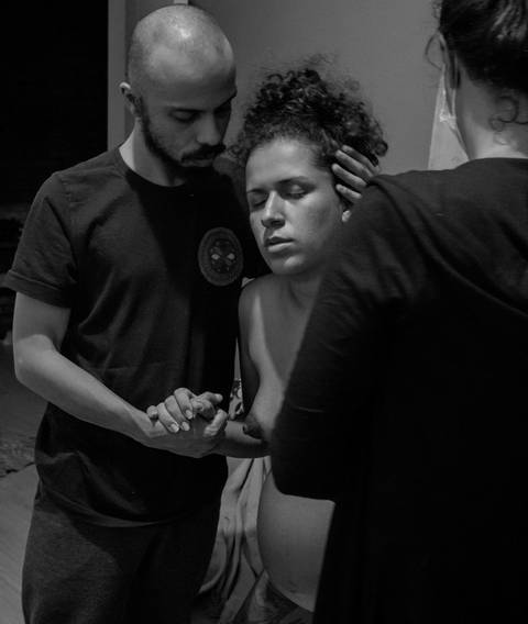 Ana com seu parceiro, em trabalho de parto humanizado em sua residência na zona sul da capital de são paulo. parto de cairo. seu parceiro lhe abraça, contribuindo para o conforto de Ana. Doula acompanha na sala.'