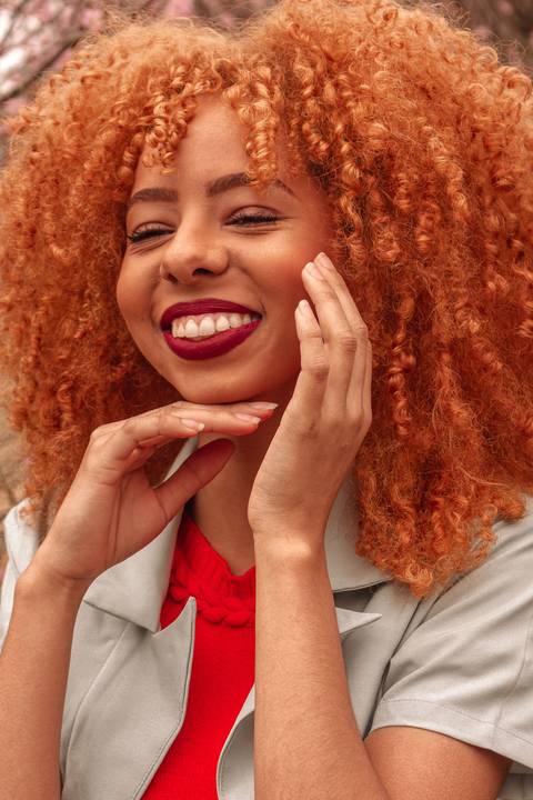 Amanda no parque do carmo, capital de são paulo, na época das cerejeiras. sorrindo com as mãos ao redor do rosto.'