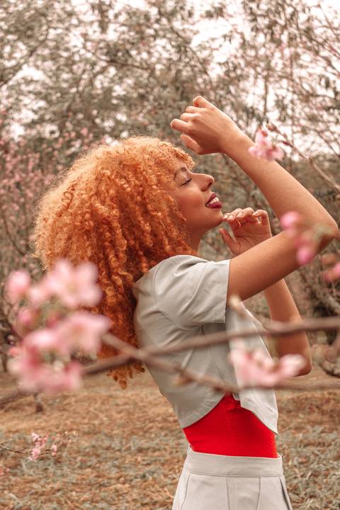 Amanda no parque do carmo, capital de são paulo, na época das cerejeiras. sorrindo, em movimento com os braços.'