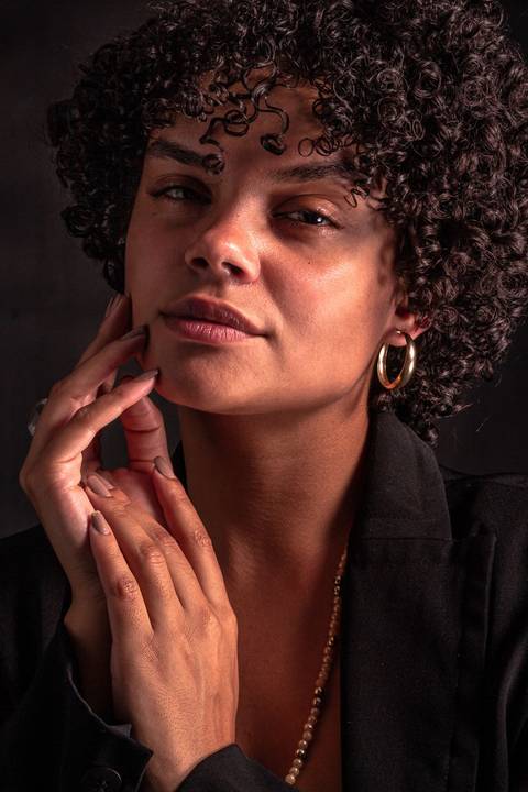 Cássia modelando em estúdio na zona norte da capital de são paulo. olhar sensual, mão próxima ao rosto, mais enquadrado. com jaqueta preta vestindo.'