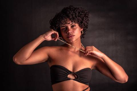 Cássia modelando em estúdio na zona norte da capital de são paulo. olhar sensual, mão próxima ao rosto, mais enquadrado. segurando e esticando colar em seu pescoço.'