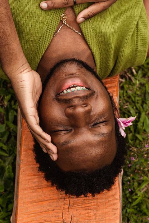 Hugo no parque do carmo, na capital de são paulo. Com uma flor na cabeça, enquanto sorri leve, deitado nos bancos coloridos.'
