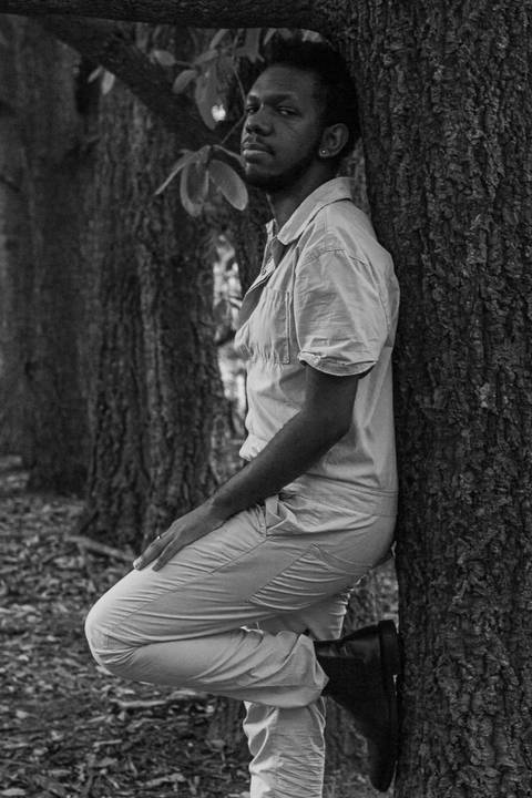 Hugo no parque do carmo, na capital de são paulo. Encostado em uma árvore, olhando em direção a câmera.'