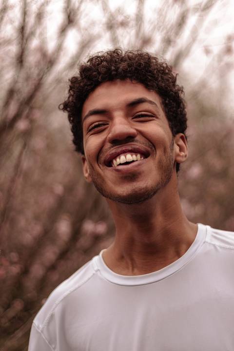 Isaque bailarino, sendo fotografado no parque do carmo na época das cerejeiras, enquanto faz movimento, sorrindo espontâneo.'