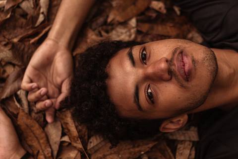Isaque em meio as árvores, época de outono no parque do carmo, folhas ao seu redor, enquadramento mais fechado, deitado sobre as folhas caídas no chão.'