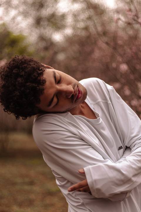 Isaque bailarino, sendo fotografado no parque do carmo na época das cerejeiras, enquanto faz movimento de dança.'