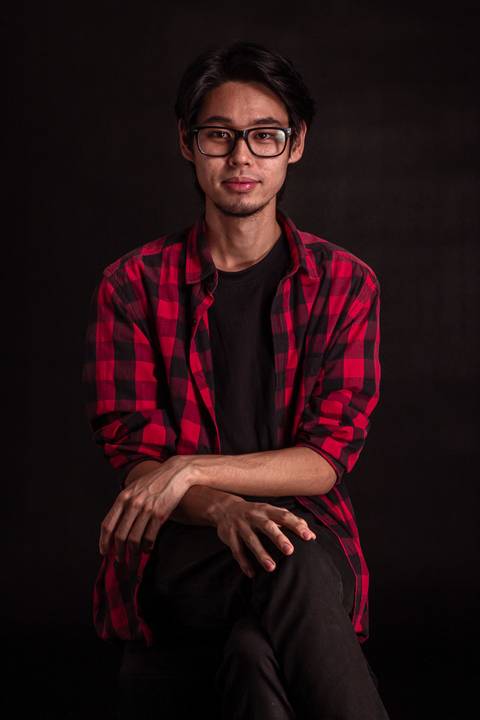 Jorge em estúdio na capital de são paulo, sentado em frente ao fundo preto, camiseta xadez, olhando em direção para a câmera.'