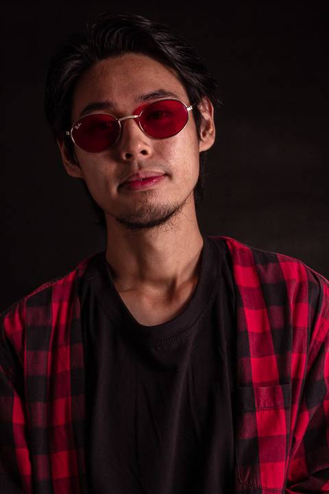 Jorge em estúdio na capital de são paulo, sentado em frente ao fundo preto, camiseta xadez, olhando em direção para a câmera, enquadramento mais próximo, óculos escuros.'