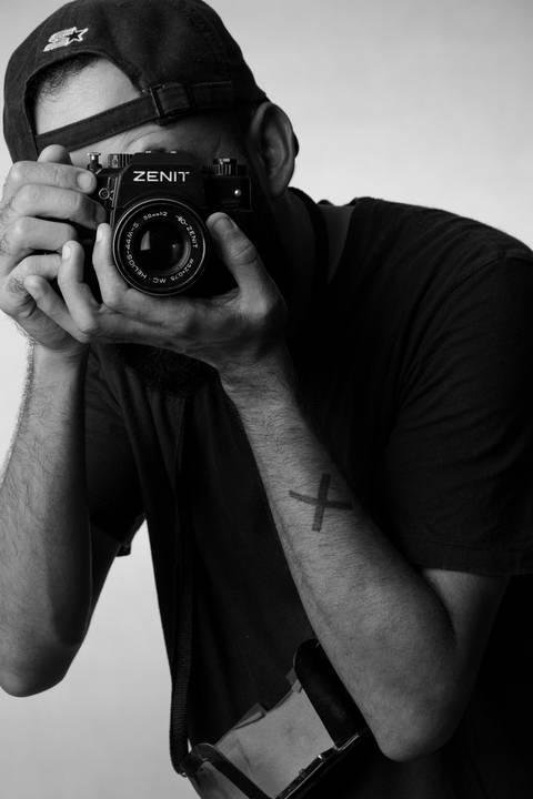 Kevin, em estúdio com fundo branco, olhando através da câmera em suas mãos, como se fosse fotografar a fotógrafa.'