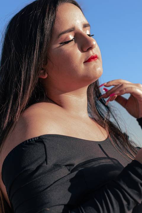Lethícia com olhos fechados, com a mão próxima ao seu rosto, com sol iluminando sua face.'