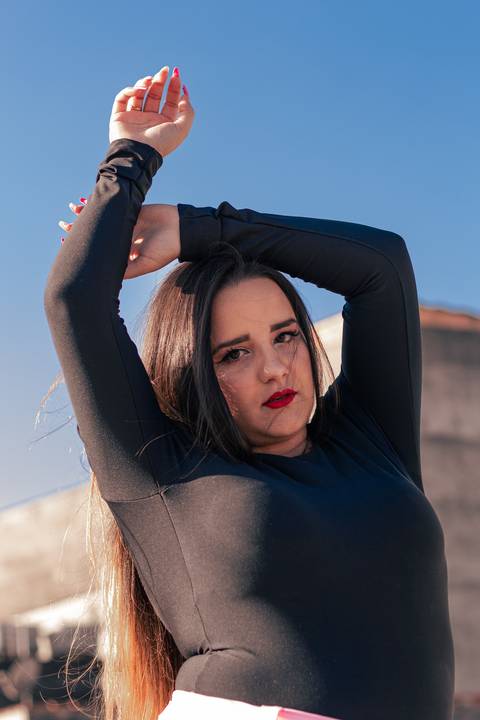 Lethícia com os braços estendidos por volta da cabeça, com o olhar direcionado para a câmera.'