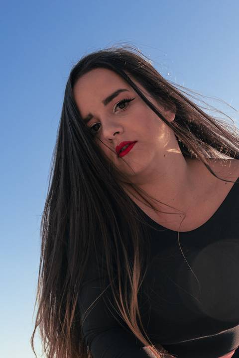 Fundo totalmente de céu azul, Lethícia sendo fotografada de baixo, cabelos soltos ao vento.'