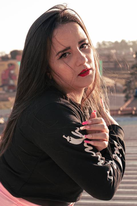 Lethícia inclinando o corpo para frente, sendo fotografada pela lateral, com cabelos ao vento, passando pelo seu rosto.'