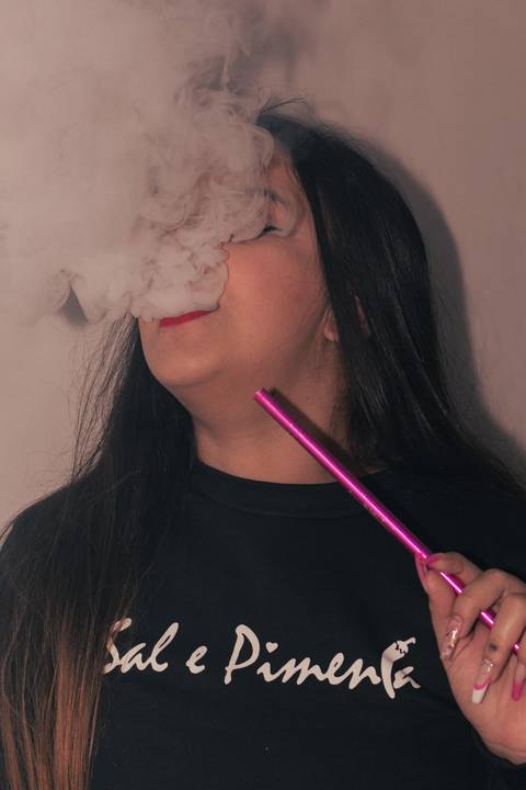 Lethicia soltando fumaça de narguilé pela boca, concentrando bastante quantidade em frente ao seu rosto.'