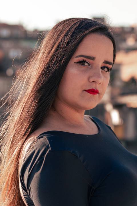 Lethícia olhando para a cãmera, com fundo de casas e céu azul.'