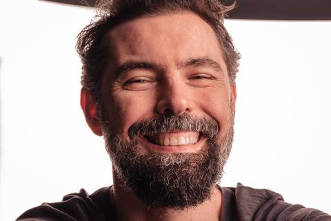 Luís sorrindo para a câmera, em estúdio com fundo branco.'