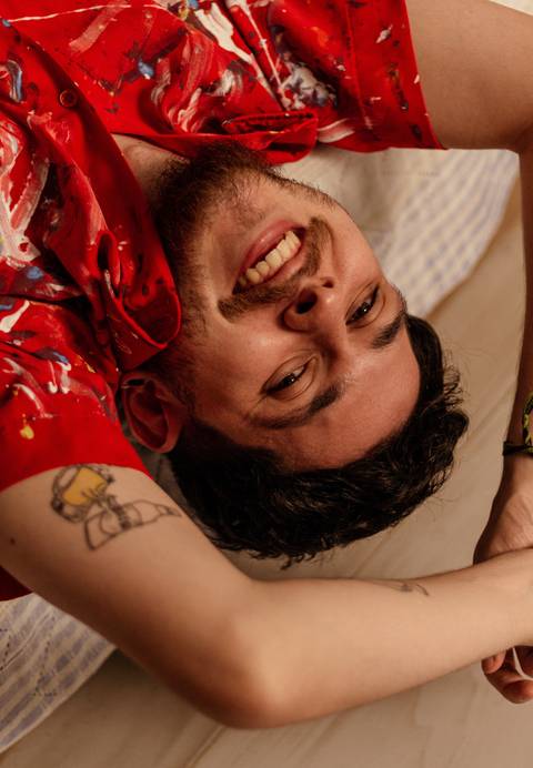 Matheus de cabeça para baixo em seu sofá, sorrindo espontâneo.'